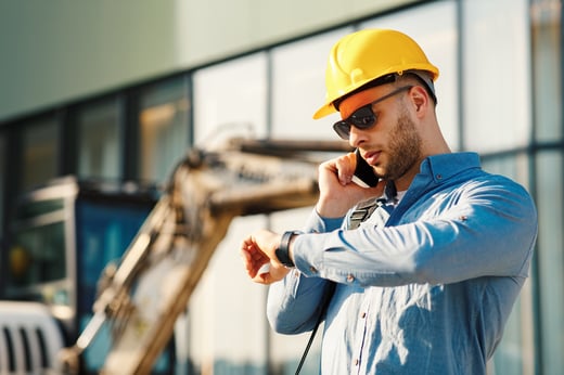 construction engineer talking on the phone and looking at his watch AdobeStock_269079228